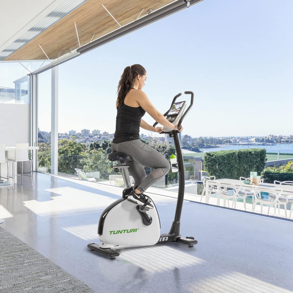 Tunturi hometrainer Vrouw in sportieve kleding zittend op Tunturi hometrainer E60 met geweldig uitzicht naar buiten.